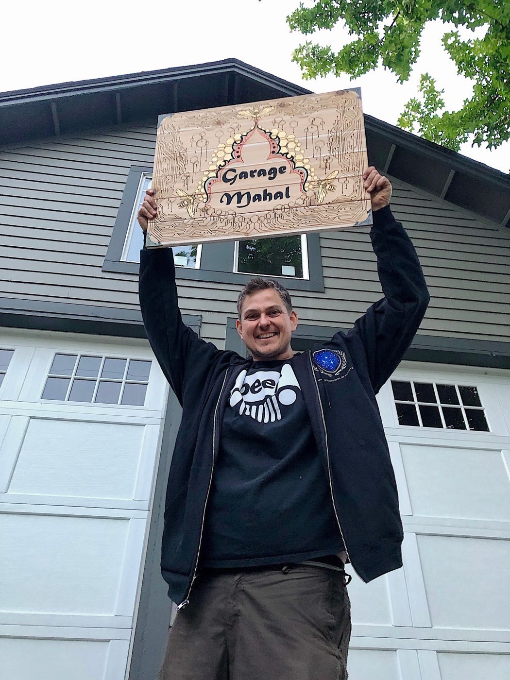 A buyer holding a custom wood burned Garage Mahal sign high above his head in front of his new white garage doors