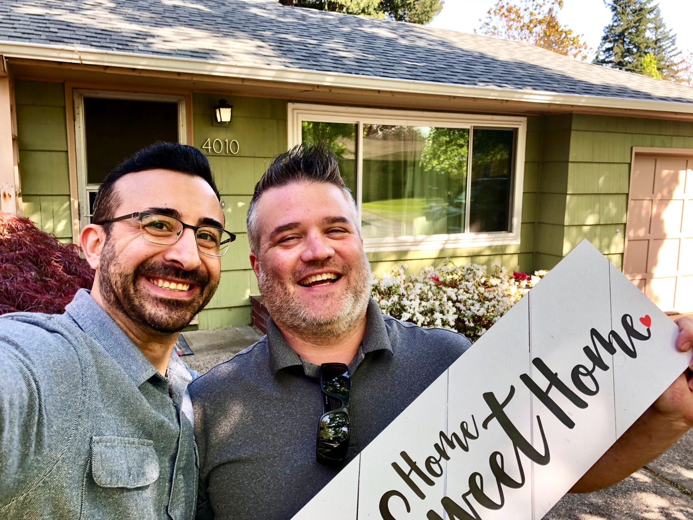 Tim taking a sunny selfie with a buyer who is tilting a large Home Sweet Home sign in front of his green ranch house
