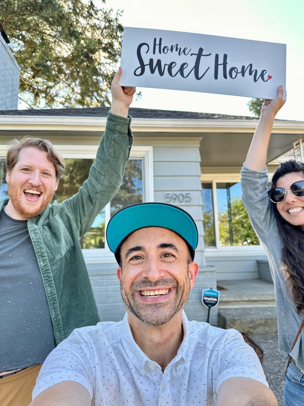 Tim taking a selfie with two buyers who are holding a Home Sweet Home sign overhead outside their new white house